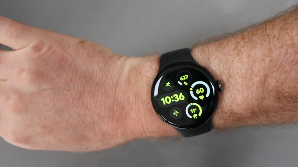 A smartwatch with a black band displays the time as 10:36 and various health metrics, worn on a person's wrist against a gray background.