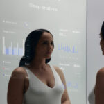 A woman looks into a smart mirror displaying sleep analysis data, including graphs and statistics. A label reads "CES Prototype.